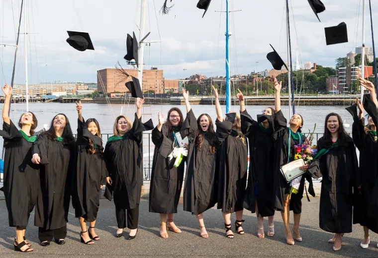 women wear black graduation robes and toss their graduation caps in the air