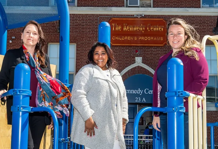 three women stand on a jungle gym with kennedy center sign in the background