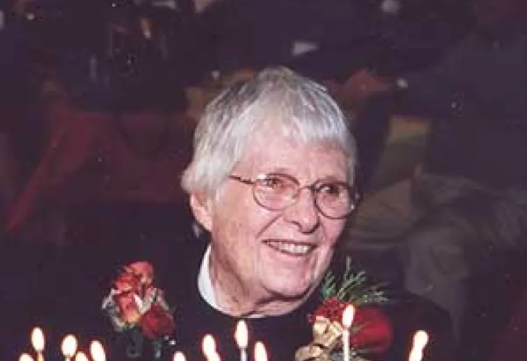 photo taken at a party - marjorie smiles over a cake with lots of candles and wears a corsage of roses