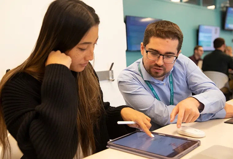 Woman with long hair points at a tablet while a man in a blue shirt looks on