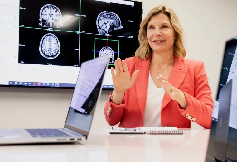 Woman sitting at a table with a brain scan image behind her