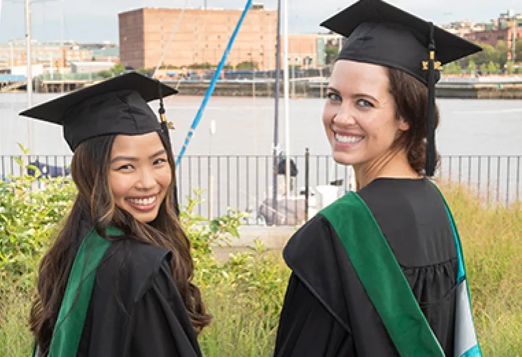 two women look over their shoulders at the camera they wear grad caps and gowns