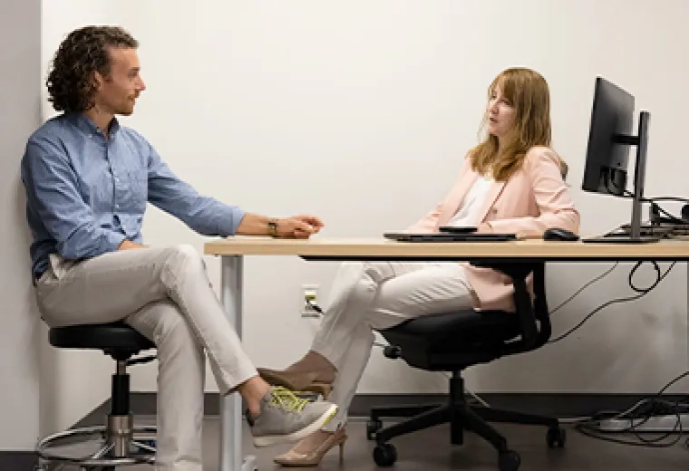 a man and woman sit and talk at a desk