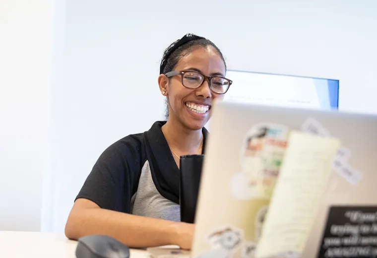 woman smiles and looks at her laptop which is covered with stickers