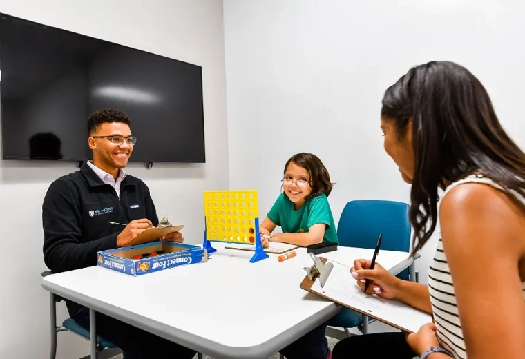 a child plays connect four with two student clinicians