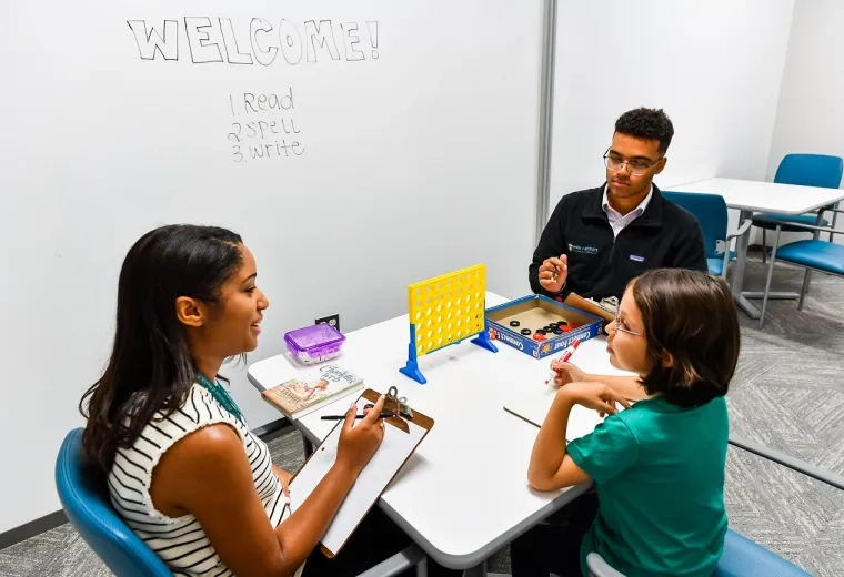 A group therapy session with two adults working with a young child on speech and language intervention techniques using games. This image is relevant to clinical practicum for SLPs and graduate speech pathology programs.