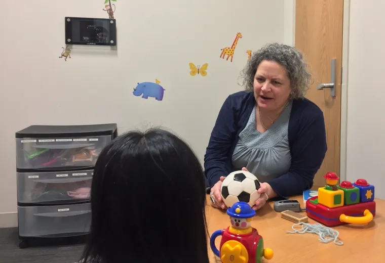 woman holds soccer ball and speaks to a child while seated at a table
