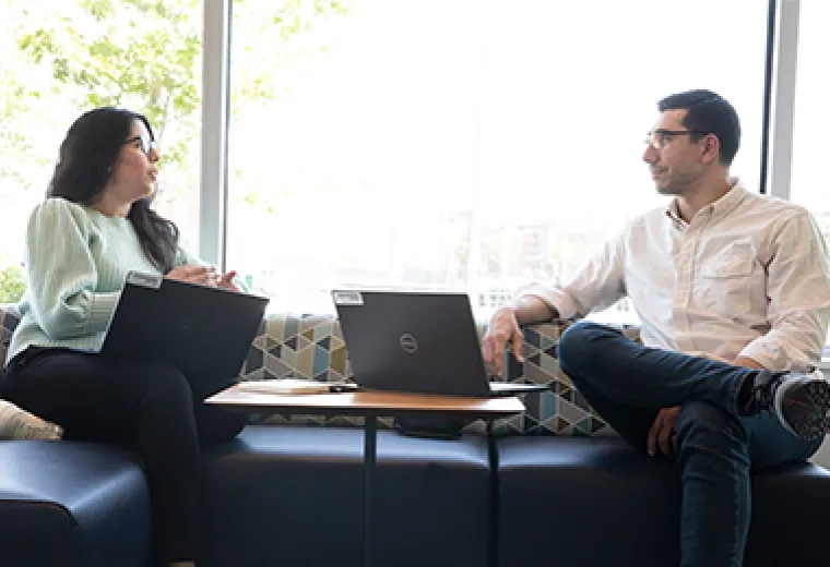 a man and woman sit and speak casually with laptops between them