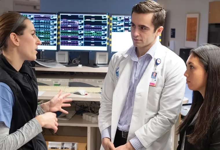 woman in scrubs speaks to man in lab coat and woman in black blazer