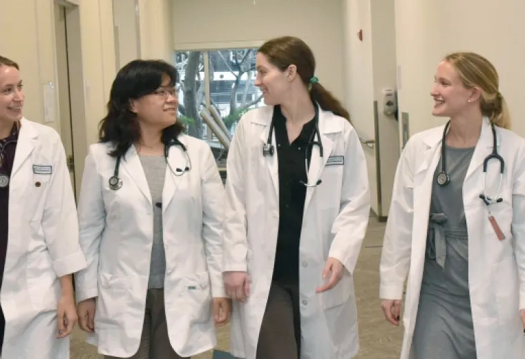 women in white coats walk down hallway