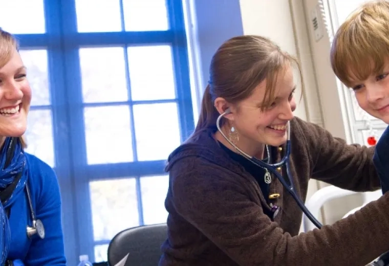 woman uses stethoscope on a boy while another smiles