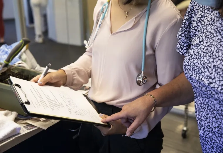 Two people fill out a form on a clipboard together. One is wearing a stethoscope 
