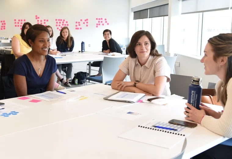 women sit around a conference room table with pink postit notes on the wall