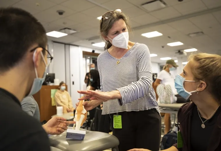 woman points to a model of a knee while two masked students look on