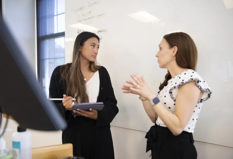 Professor gestures to a student in front of a white board