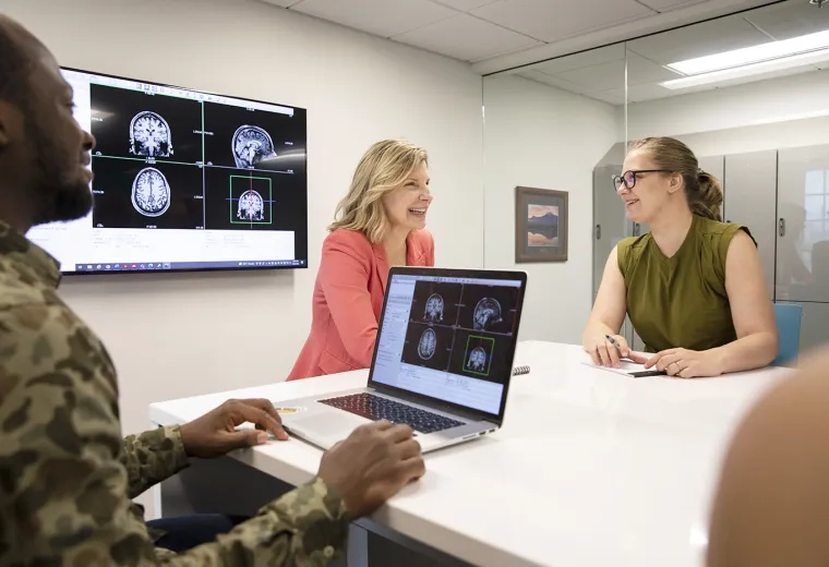 two women and a man converse and look at brain scans on screens