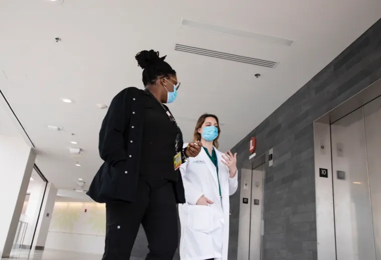 Two nurses wearing masks while walking down a hallway