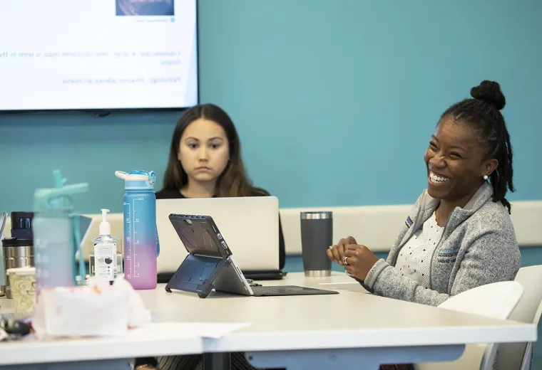 woman laughs at something off camera while she uses her tablet at a table
