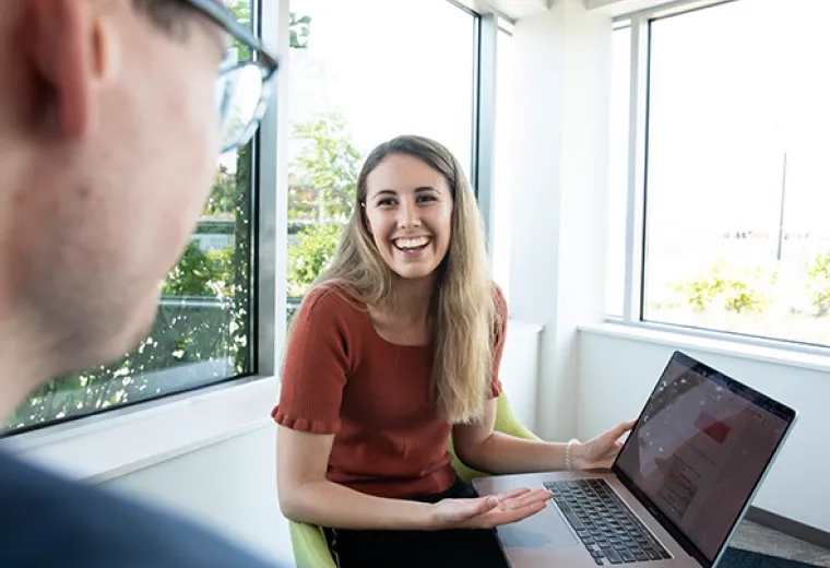 Woman gestures to laptop in questioning fashion to man in foreground