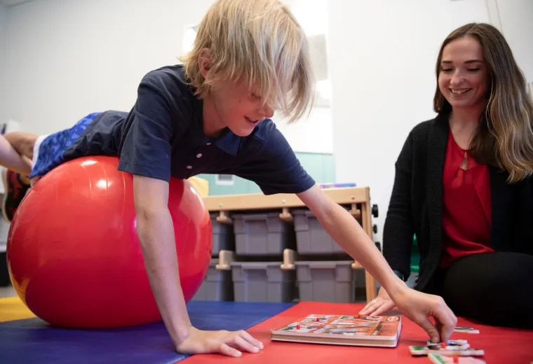 Occupational therapy student assisting a child during therapy using a stability ball and educational game in the Doctor of Occupational Therapy program.