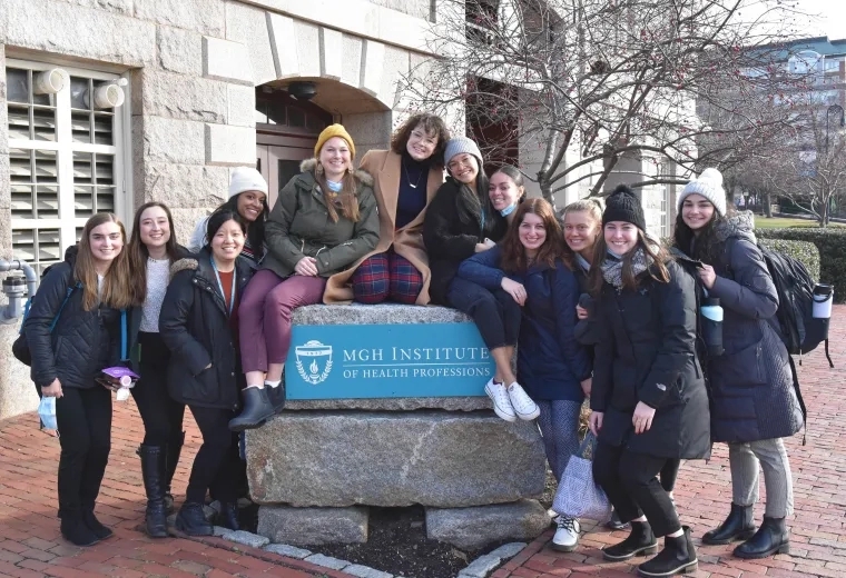 female students sit on a rock that says mgh institute of health professions