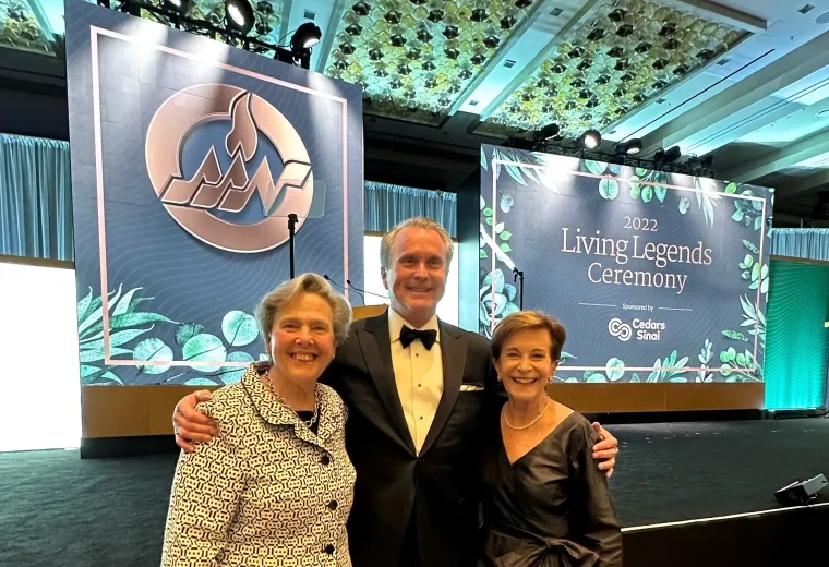 man stands in middle with arms around two women dressed in formal attire