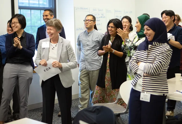 a group of men and women, some Asian and some in hijabs smile and laugh in a classroom setting