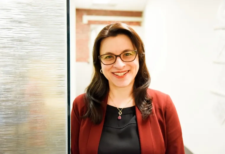 profile photo of Joanna wearing a red cardigan and glasses leaning against a glass wall and smiling