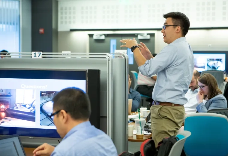 man gestures above students and large screens