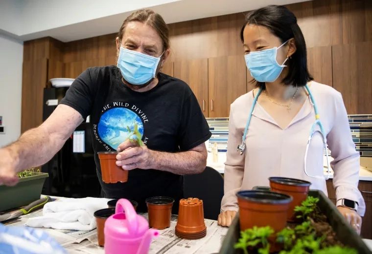 a woman in a stethoscope looks on while an older man plants a plant