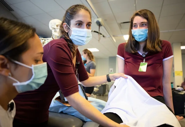 woman holds up cloth in front of another woman on an exam table