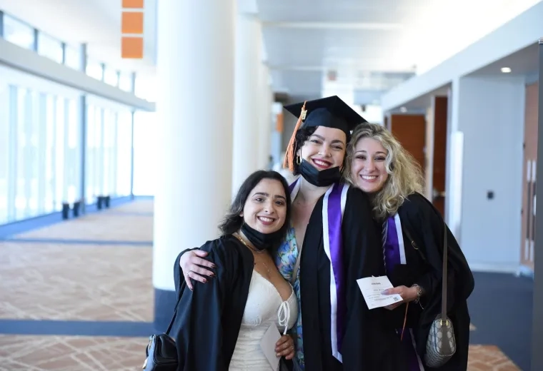 three women stand with their arms around each other in graduation caps and gowns