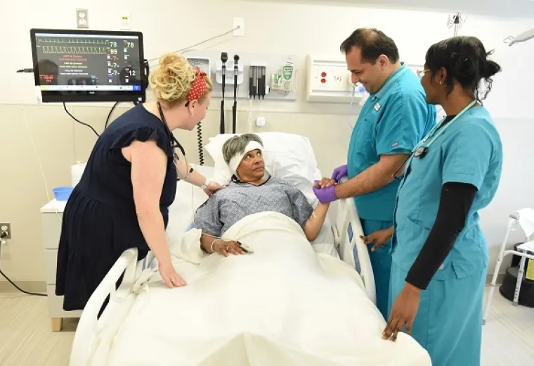 a man and woman in scrubs hold the hand of an older woman in bed while a woman in a dress speaks