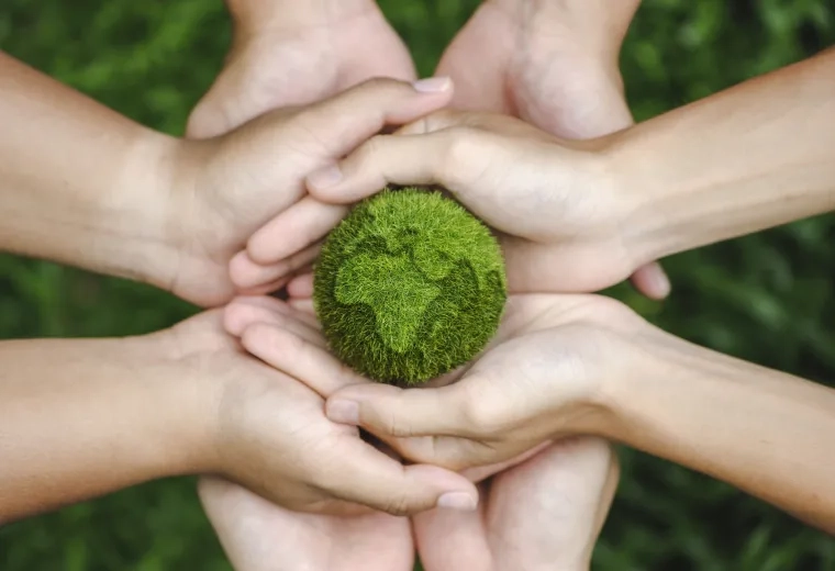 hands holding a tiny earth made of green grass