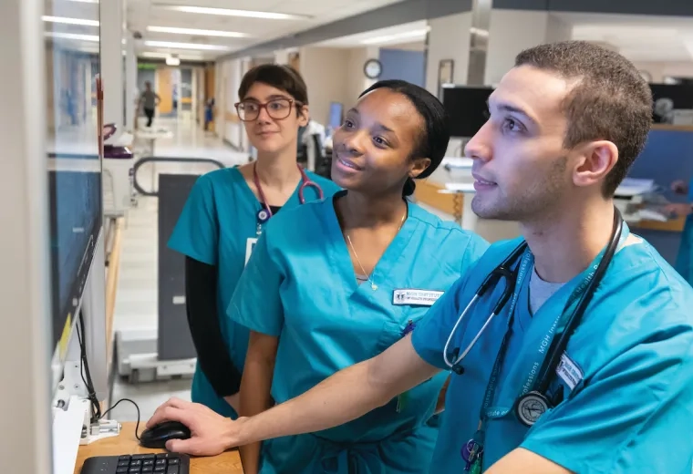 three people in scrubs look at computer monitor