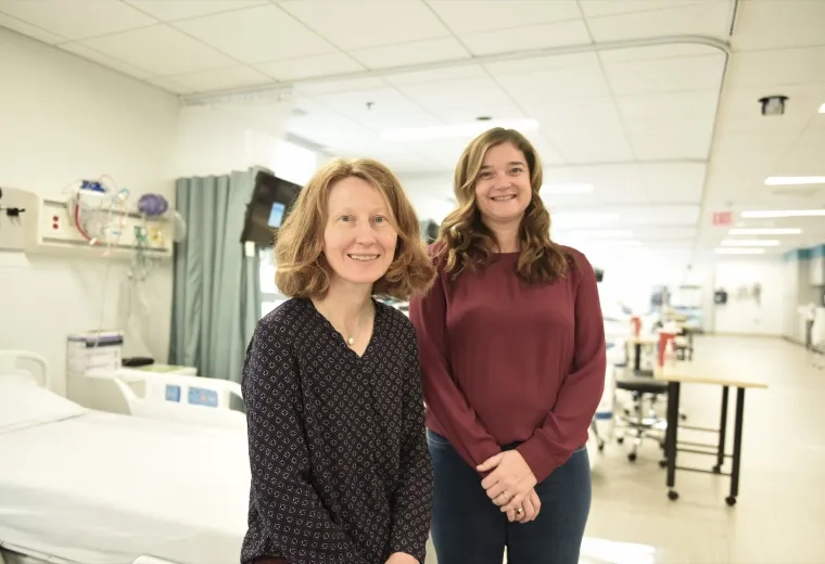 woman sits on stretcher in hospital hallway while another woman stands behind