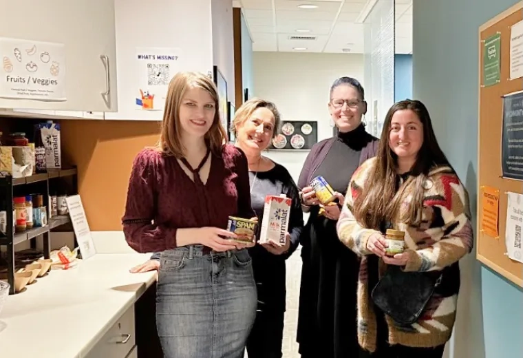 women pose with cans of food in their hands next to a cabinet