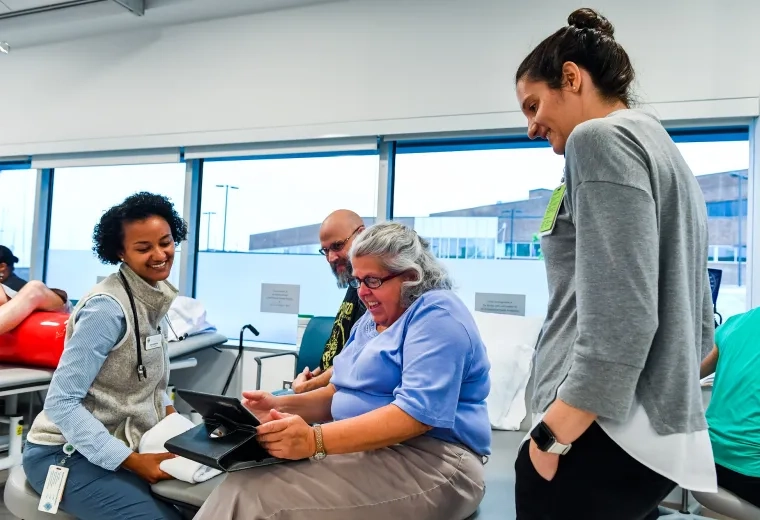 jane, seated, looks at a tablet while students stand around her