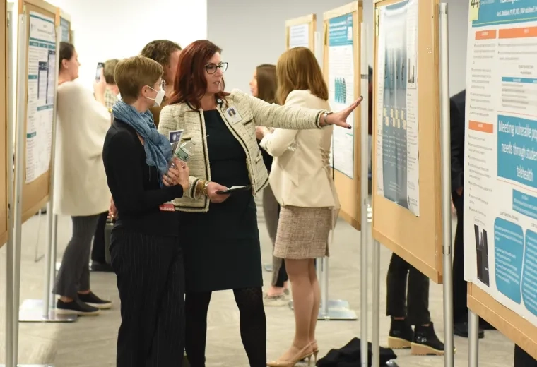 woman points to giant bulletin board with poster on it while another woman looks on