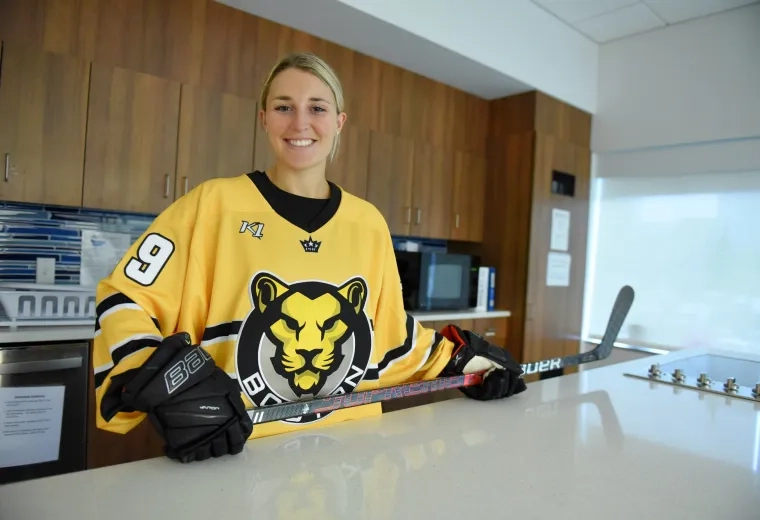 sammy stands at the occupational therapy kitchen counter in her yellow hockey jersey holding a hockey stick