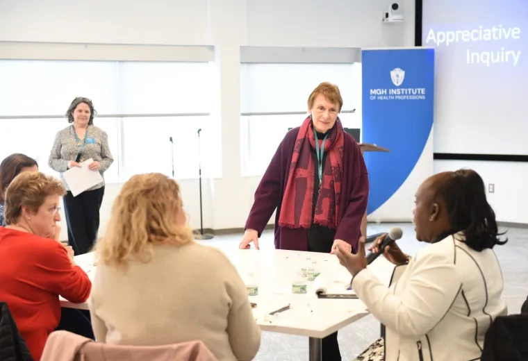 women in a bright room listen to a woman seated holding a microphone