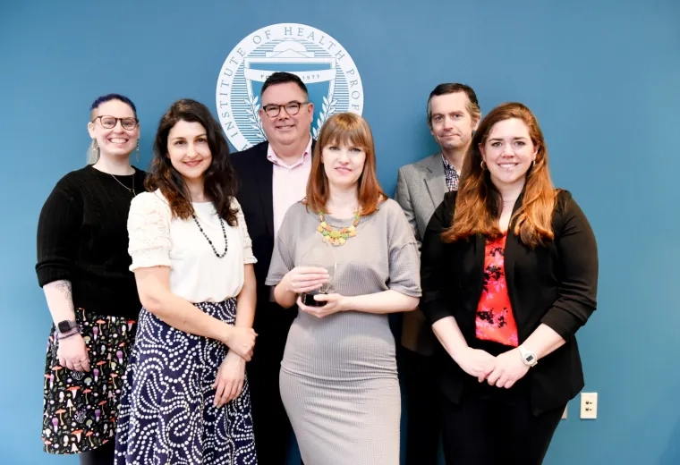 group of people smile, woman in front holds tear-drop shaped glass award