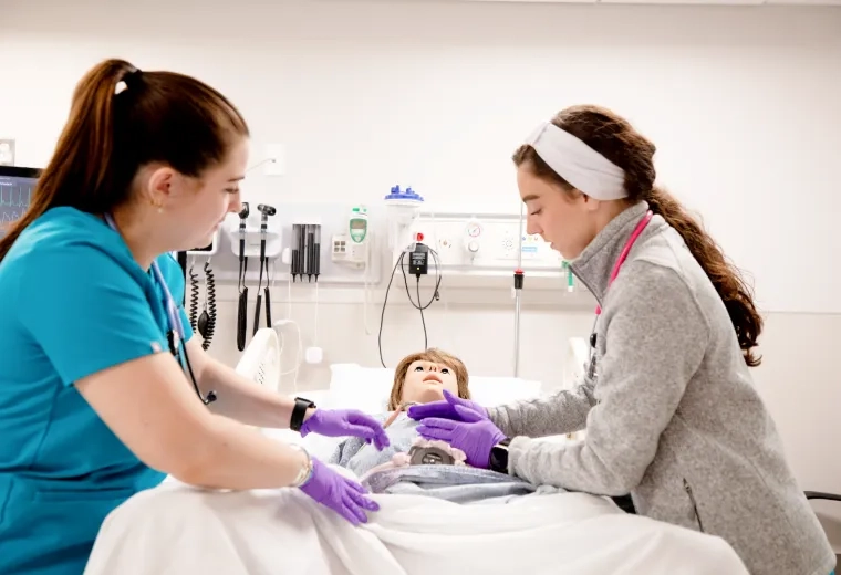 Two nursing students working with a simulation manikin in-between them..