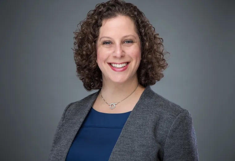 rachel has curly brown hair and wears a grey blazer