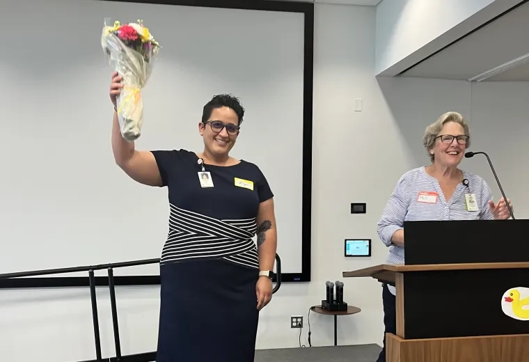 angela wears a black and white striped dress and holds a bouquet of flowers aloft on a stage