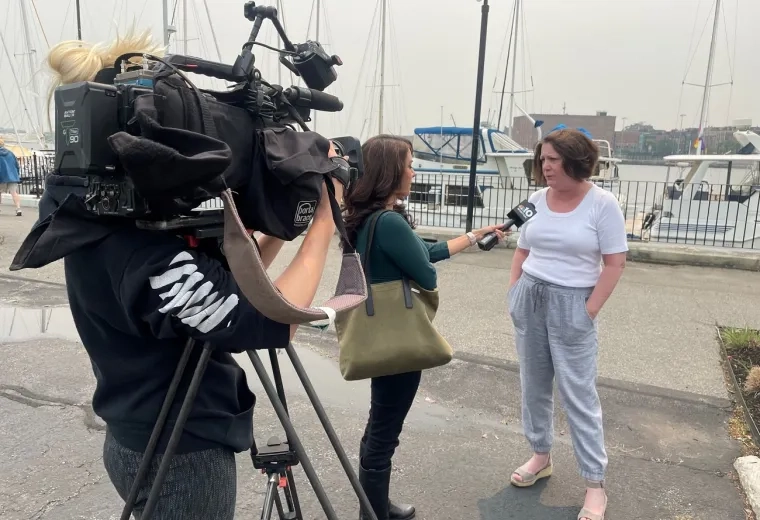 news crew with microphone and camera stand and speak to sue who wears a white top and grey pants