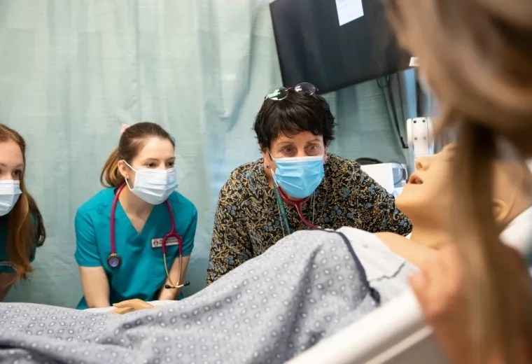 People in masks looking at manikin in a room.