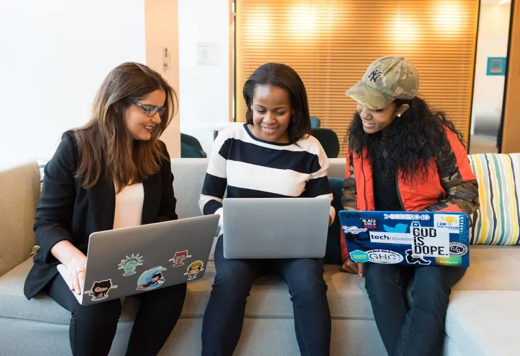 three women sit on a couch with their laptops