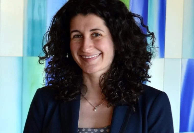 yelena wears a blue blazer and has dark wavy hair