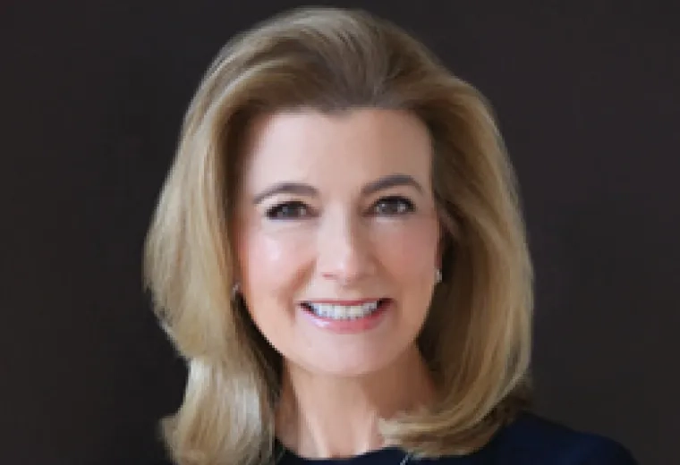 woman with blond hair styled in a wave back from her head wearing a navy top and silver necklace